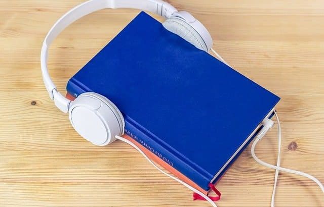 livro azul sobre mesa de madeira com headphone branco em volta da capa
