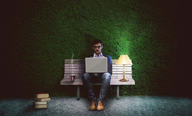 homem sentado em banco de madeira com notebook no colo
